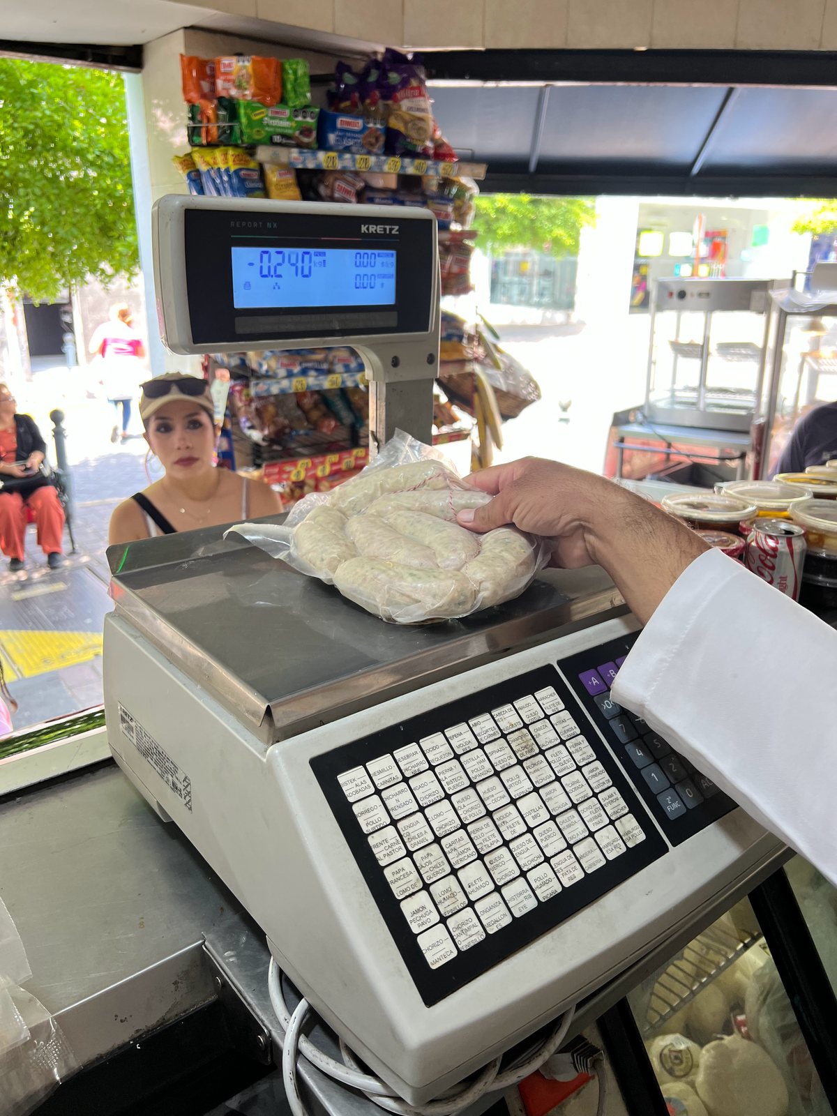 Una mano coloca el pedido sobre la báscula del mostrador mientras la clienta lo mira desde el otro lado.