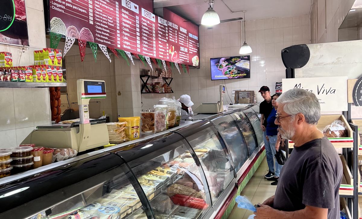 El mostrador de El Rodeo hoy: la vitrina llena, las pizarras de charcutería al fondo y clientes esperando su pedido.