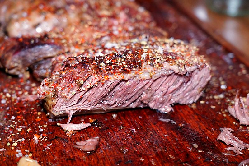 Un corte ya asado y rebanado sobre la tabla, con la costra dorada y la sal y la pimienta todavía encima.